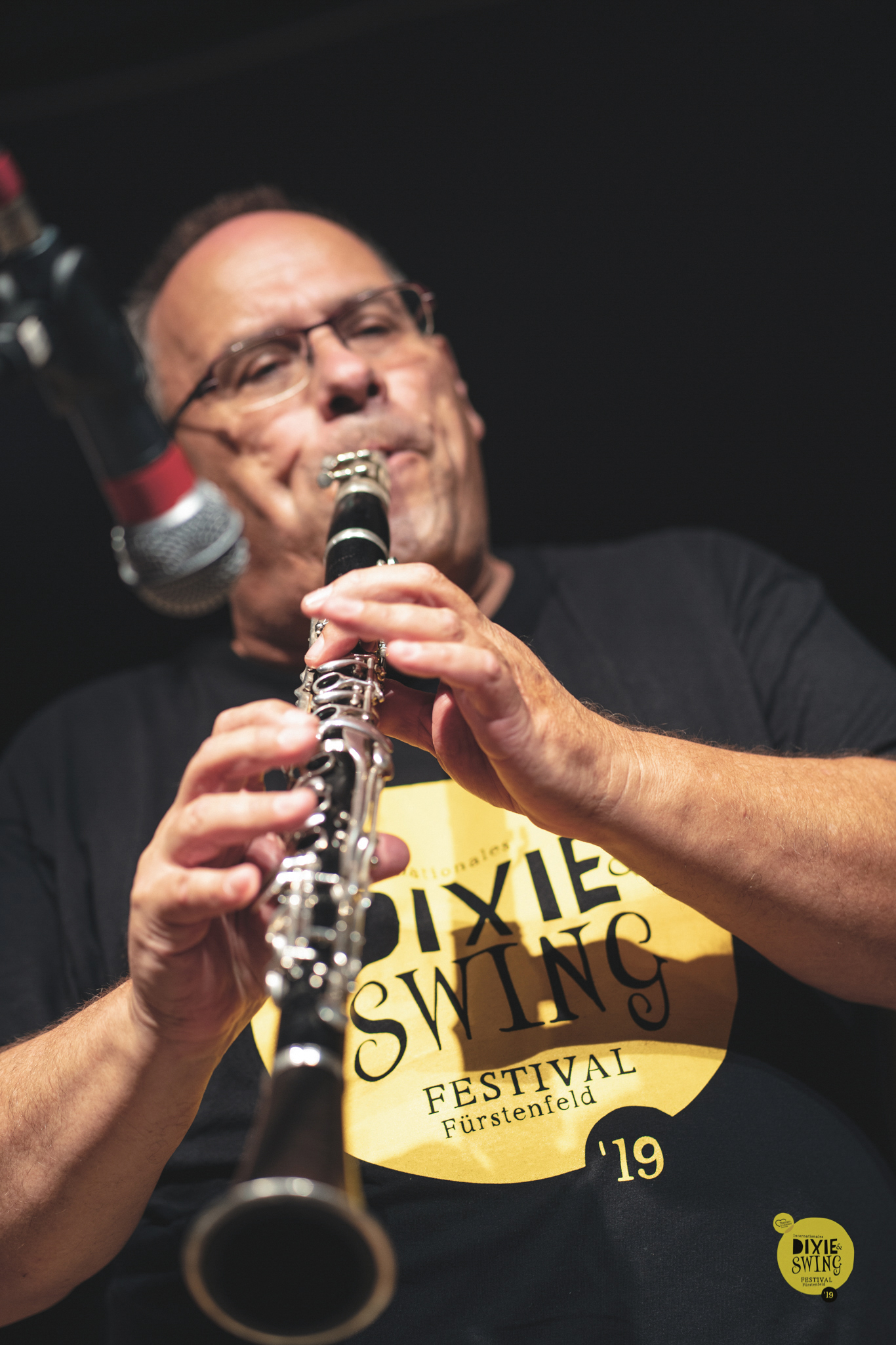 Ein Mann mit Brille spielt auf der Bühne eine Klarinette, vor ihm ein Mikrofon und ein "Dixie Swing Festival"-Shirt.