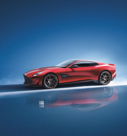 Ein schnittiger roter Sportwagen mit schwarzen Rädern parkt auf einer glänzenden Oberfläche mit blauem Farbverlauf, der das Bild des Autos widerspiegelt.