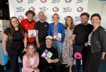 Neun Menschen, die beim Ö3-Podcast-Festival zusammen lächeln, mit einem Banner vom Haus der Stillen Sanierung 2026 im Hintergrund.