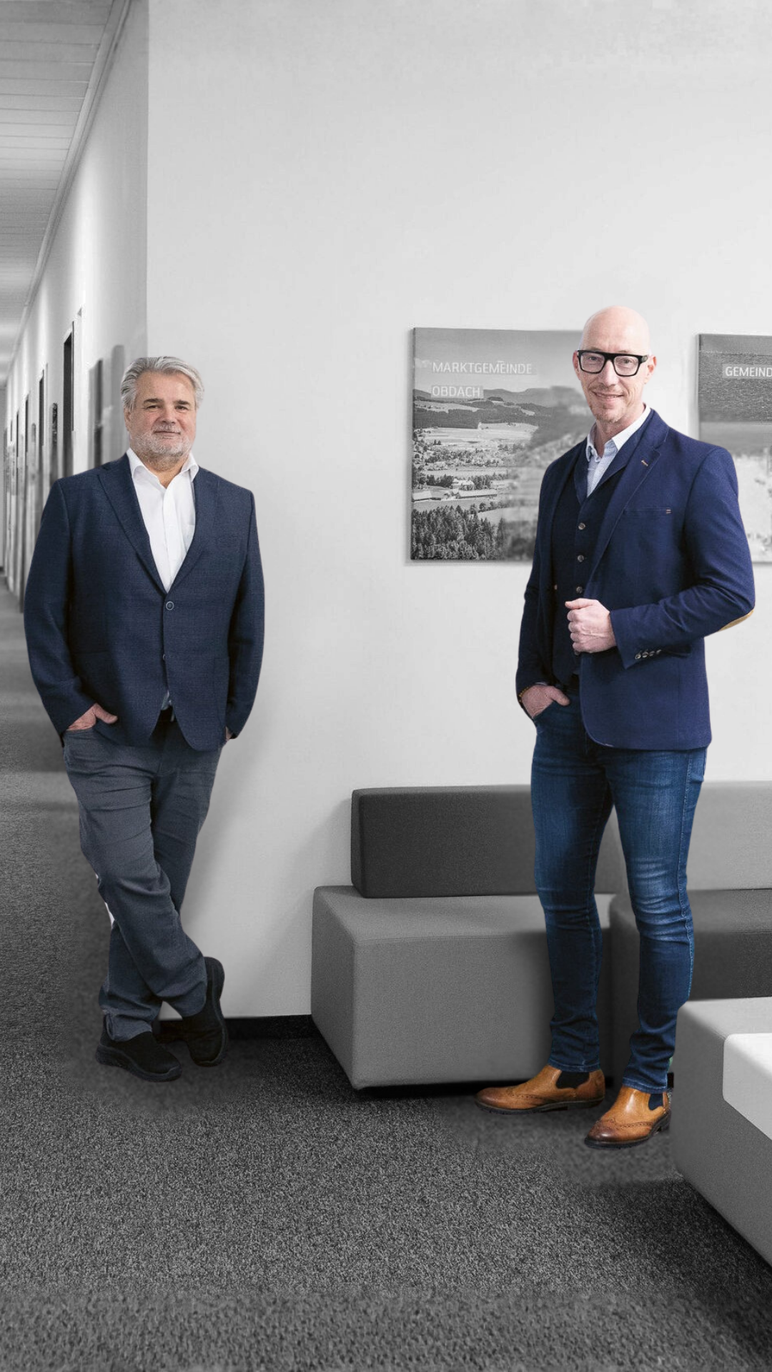 Zwei Männer in Anzügen stehen in einem modernen Büro mit kunstvollen Gemälden hinter ihnen.
