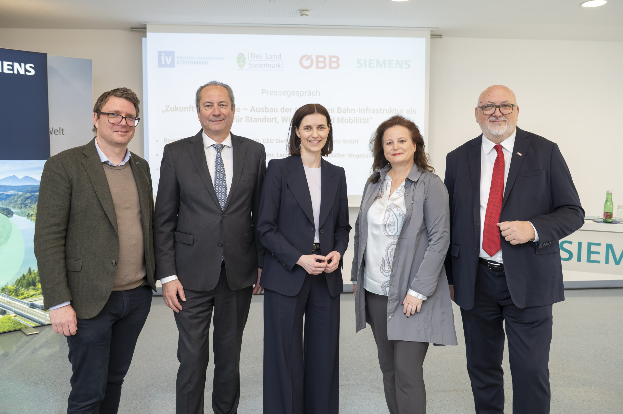 Fünf Personen in Geschäftskleidung lächeln für ein Gruppenfoto bei einer Presseveranstaltung zum Thema "Finanzbetrug erkennen und vermeiden", hinter ihnen die Logos von Siemens und den ÖBB.