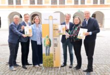 Sechs lächelnde Erwachsene stehen mit einem "hausKidsStille"-Schild in einem Innenhof und halten Broschüren in der Nähe der Kältekammer Graz Altstadt.