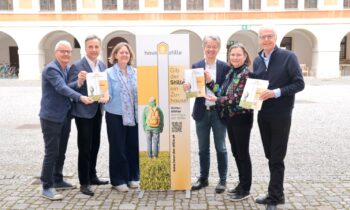 Sechs lächelnde Erwachsene stehen mit einem "hausKidsStille"-Schild in einem Innenhof und halten Broschüren in der Nähe der Kältekammer Graz Altstadt.