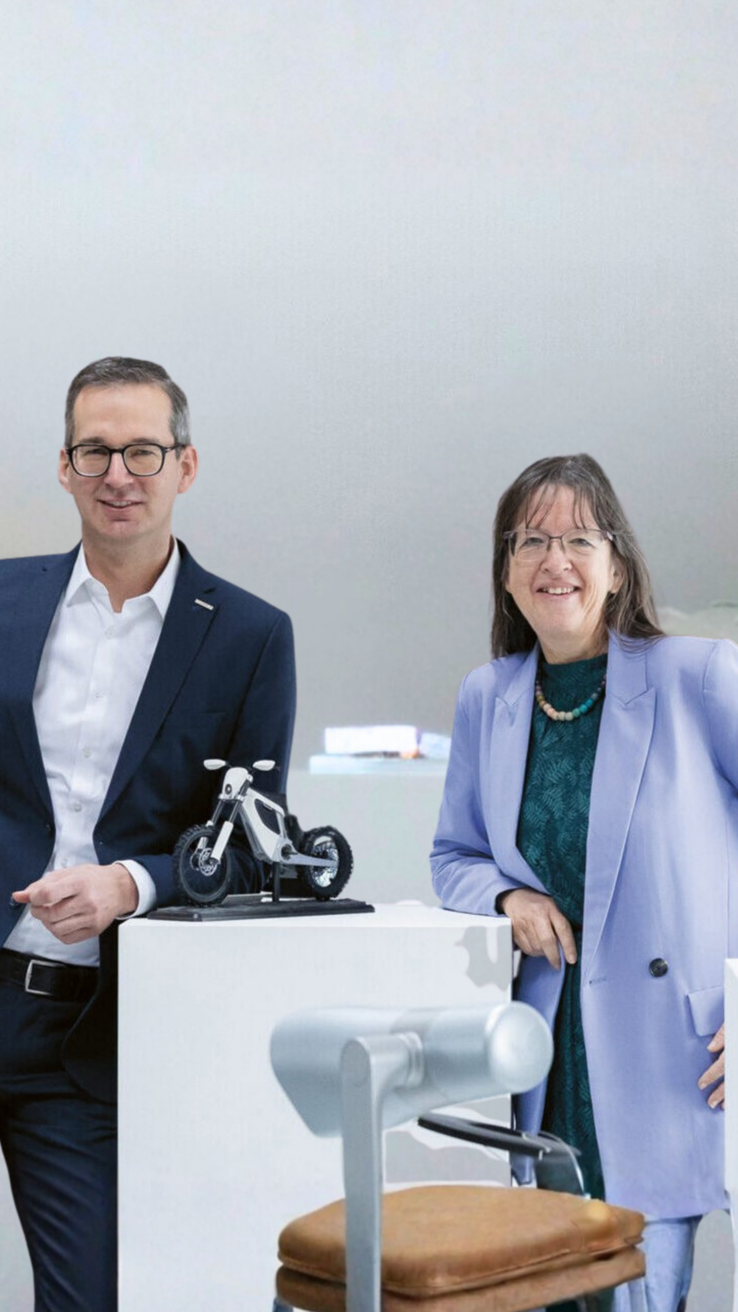Zwei Personen in Business-Kleidung stehen neben einem kleinen Motorradmodell.