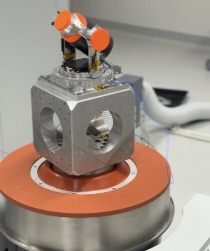 Ein metallisches wissenschaftliches Instrument mit orangefarbenen Akzenten steht auf einem Podest