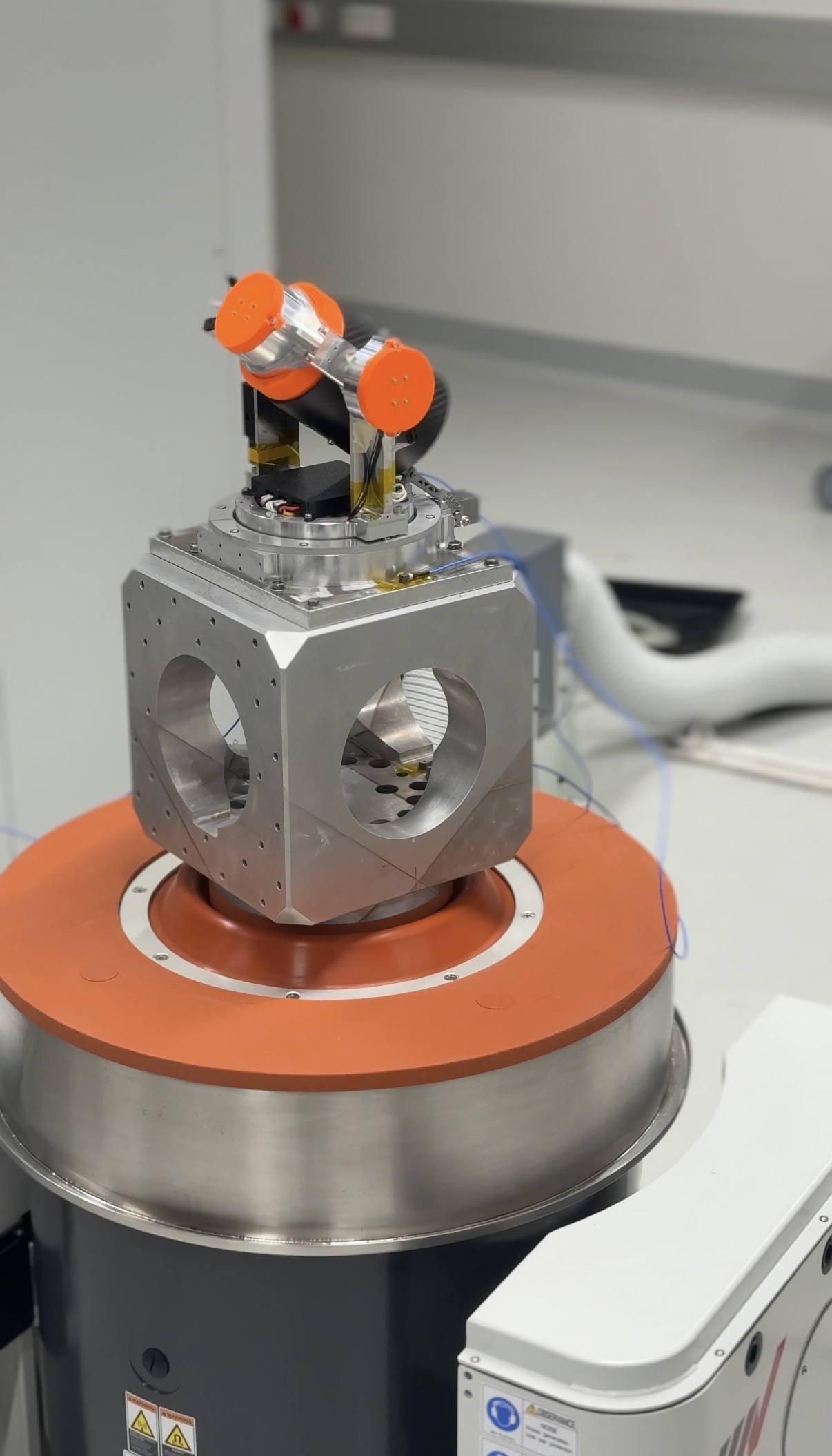 Ein metallisches wissenschaftliches Instrument mit orangefarbenen Akzenten steht auf einem Podest