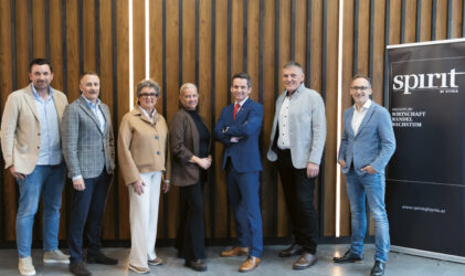 Sieben professionell gekleidete Menschen stehen lächelnd in einer Reihe neben einem "Spirit of Styria"-Banner und einer Holztafelwand.