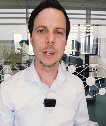 Ein Mann im weißen Hemd mit einem Mikrofon steht in einem modernen Büro