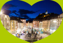 Ein herzförmiger Rahmen zeigt den Grazer Hauptplatz bei Nacht und kündigt den Führungswechsel der steirischen Seilbahnen am 5. Mai 2026 an.