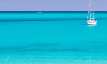 Ein einsames Segelboot schwimmt auf ruhigem, klarem türkisfarbenem Wasser unter einem strahlend blauen Himmel, mit dem Text "GRAWE Bilanz 2025 spirit" in der Ecke.