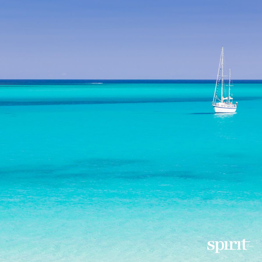 Ein einsames Segelboot schwimmt auf ruhigem, klarem türkisfarbenem Wasser unter einem strahlend blauen Himmel, mit dem Text "GRAWE Bilanz 2025 spirit" in der Ecke.