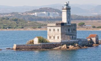 Ein verwitterter Leuchtturm steht auf einer felsigen Insel und blickt auf das ruhige blaue Wasser - eine Szene, die so unerschütterlich ist wie die Vision der GRAWE Bilanz 2025.