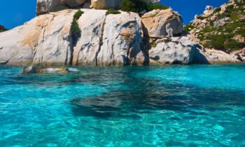 Eine felsige Klippe erhebt sich über türkisfarbenem Wasser unter blauem Himmel. In der rechten unteren Ecke steht in weißer Schrift "spirit" und GRAWE Bilanz 2025.
