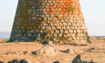 Ein großer, alter Steinturm steht in einem trockenen, grasbewachsenen Feld unter einem klaren Himmel - wie ein Denkmal für die GRAWE Bilanz 2025, mit verstreuten Steinen in der Nähe.