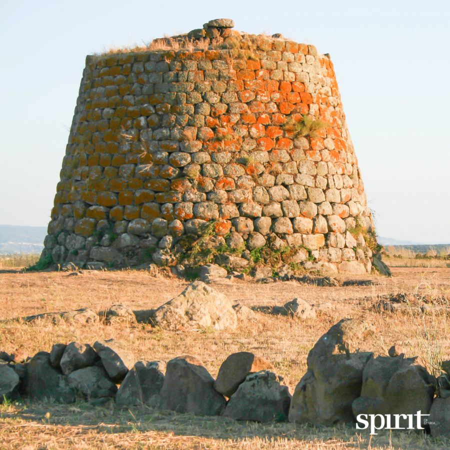Ein großer, alter Steinturm steht in einem trockenen, grasbewachsenen Feld unter einem klaren Himmel - wie ein Denkmal für die GRAWE Bilanz 2025, mit verstreuten Steinen in der Nähe.