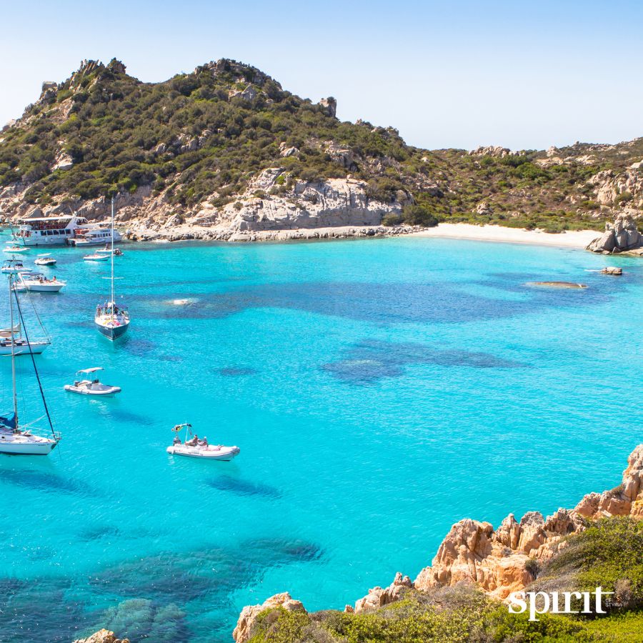Türkisfarbene Bucht mit Segelbooten, Yachten, felsiger Küste und grünen Hügeln unter blauem Himmel. In der rechten unteren Ecke erscheint die GRAWE Bilanz 2025.