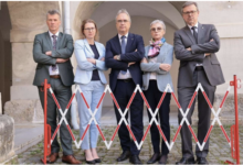 Fünf Erwachsene in Geschäftskleidung stehen mit verschränkten Armen hinter einer Schranke der GRAWE Bilanz 2025 und posieren vor einer gewölbten Gebäudehülle.