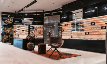 Modernes Brillengeschäft mit stilvollen Stühlen, dekorativen Pflanzen und Auslagen von Designer-Brillenmarken in Holzregalen.