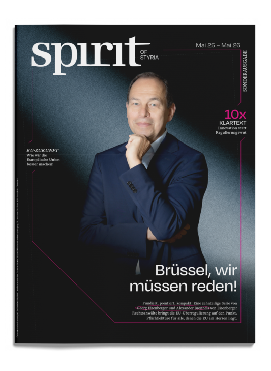 Auf dem Titelblatt des Magazins „Spirit of Styria“ – mit deutschem Text und dunklem Hintergrund – steht ein Mann im Anzug selbstbewusst da und stützt die Hand am Kinn.
