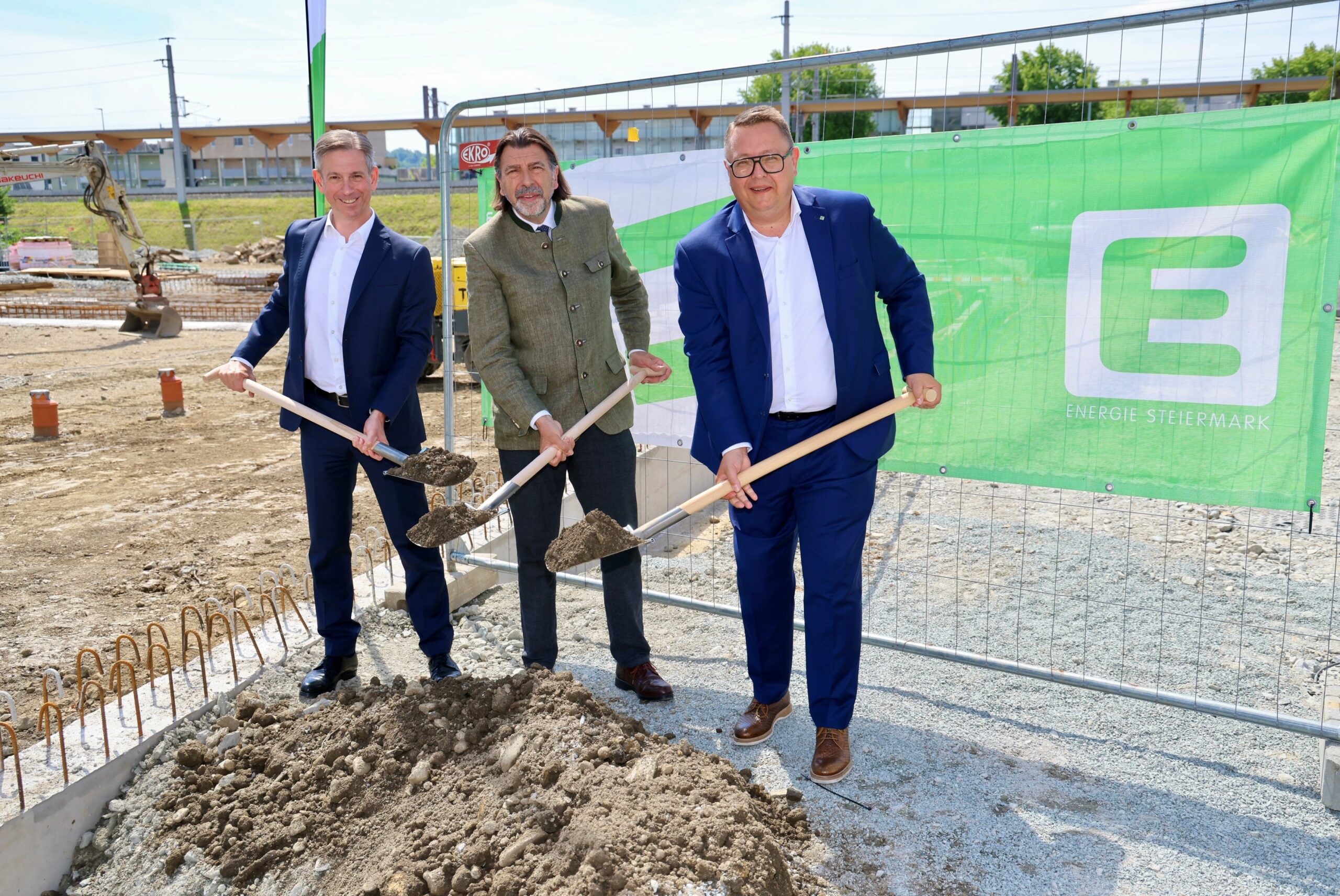Drei Männer in Anzügen machen den ersten Spatenstich für den Glasfaserausbau Steiermark. Sie stehen vor einem grünen "Energie Steiermark"-Banner auf der Baustelle.