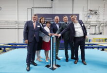 Sechs Personen in Geschäftskleidung feiern „125 Jahre Siemens in der Steiermark“ – lächelnd drücken sie in einer industriellen Umgebung einen Knopf auf einem Podium.