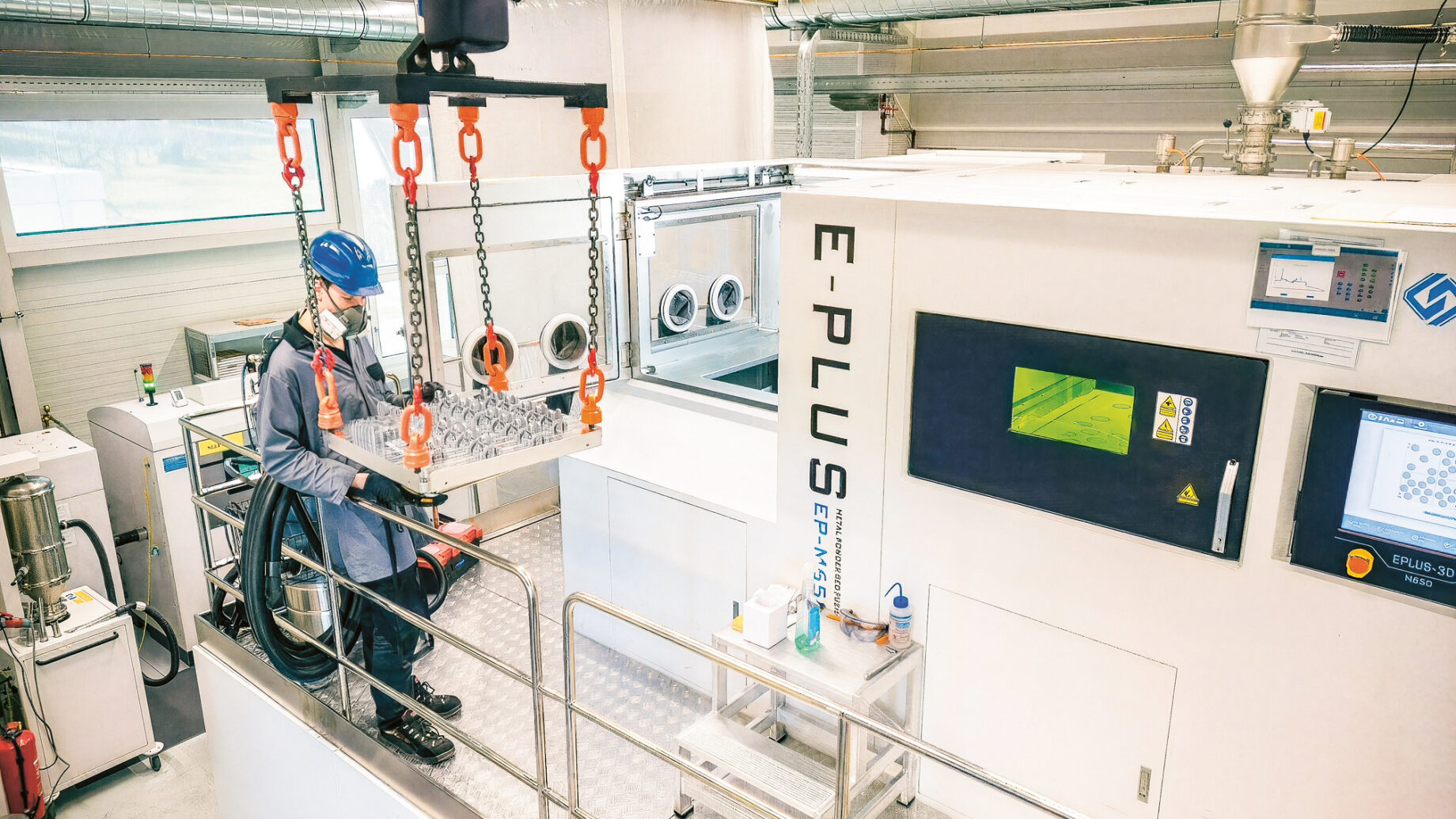 Ein Arbeiter in Schutzkleidung bedient Maschinen in einer Hightech-Industrieanlage mit Schalttafeln und Geräten mit der Aufschrift "E-PLUS".