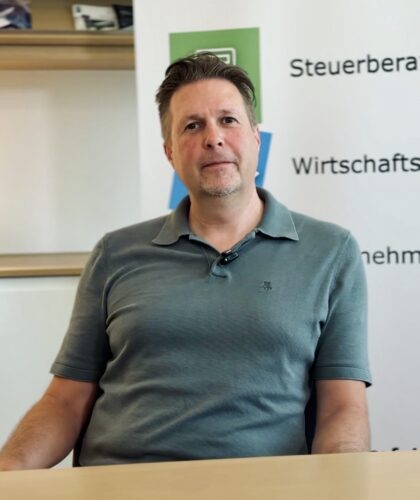 Ein Mann in einem grünen Polohemd sitzt an einem Schreibtisch.