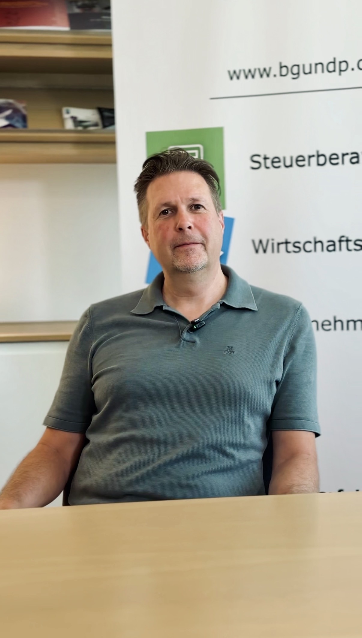 Ein Mann in einem grünen Polohemd sitzt an einem Schreibtisch.