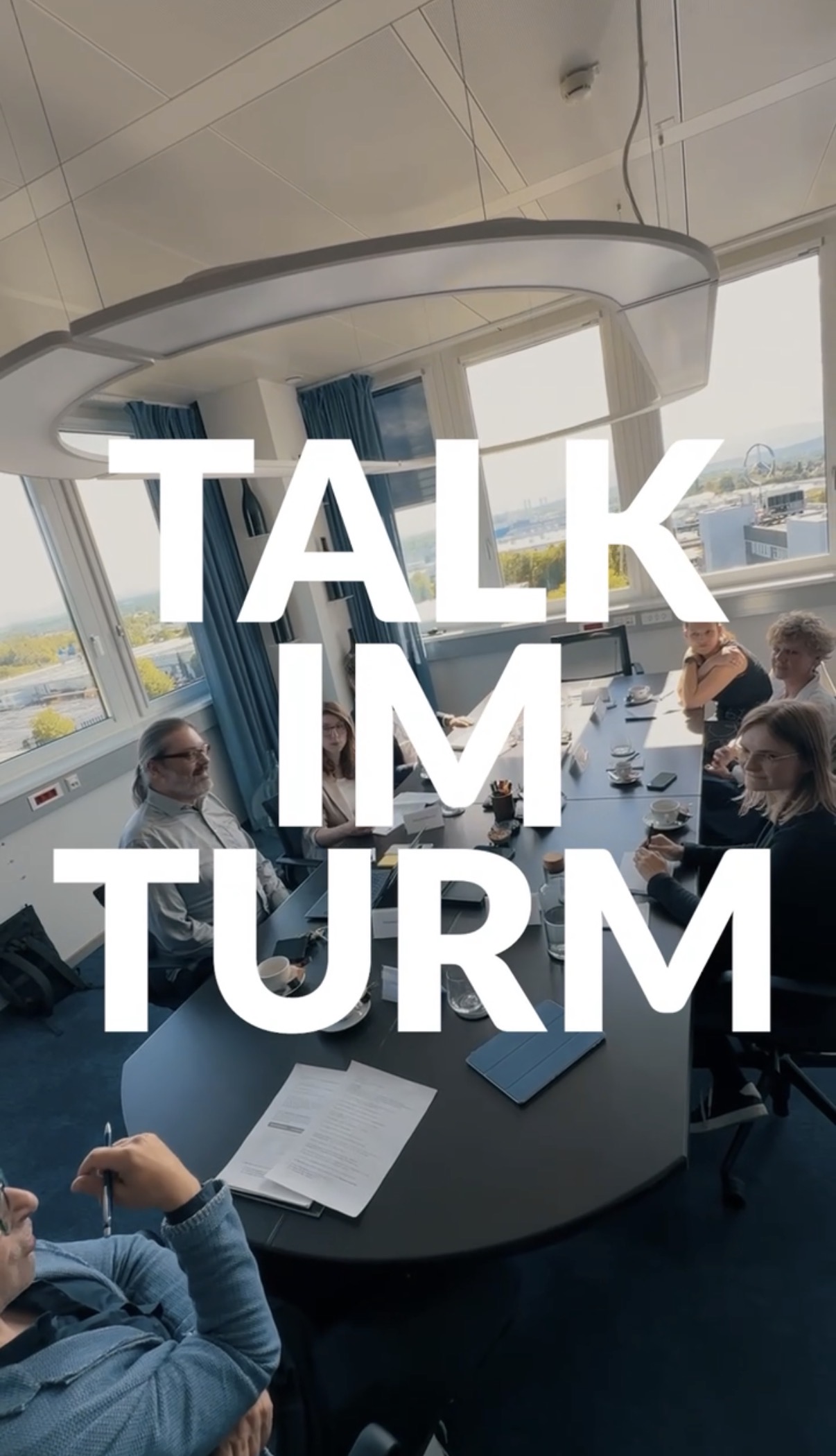 Personen an einem Konferenztisch in einem Besprechungsraum; der fettgedruckte Text lautet „TALK IM TURM“