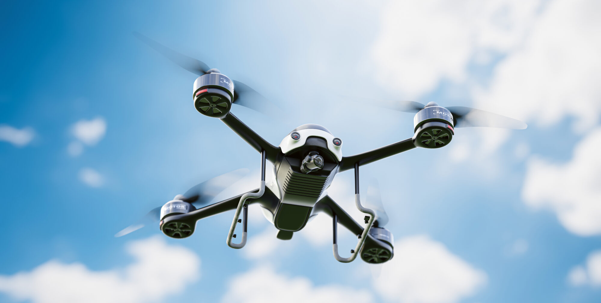 Eine schwarze Quadrocopter-Drohne fliegt vor einem blauen Himmel mit vereinzelten weißen Wolken.