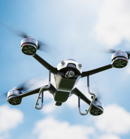 Eine schwarze Quadrocopter-Drohne fliegt vor einem blauen Himmel mit vereinzelten weißen Wolken.