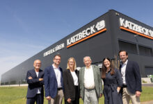 Sechs Personen in Geschäftskleidung lächeln an einem sonnigen Tag vor dem modernen Katzbeck-Gebäude - dem Sitz von Katzbeck Fenster, Testsieger bei Markentreue.