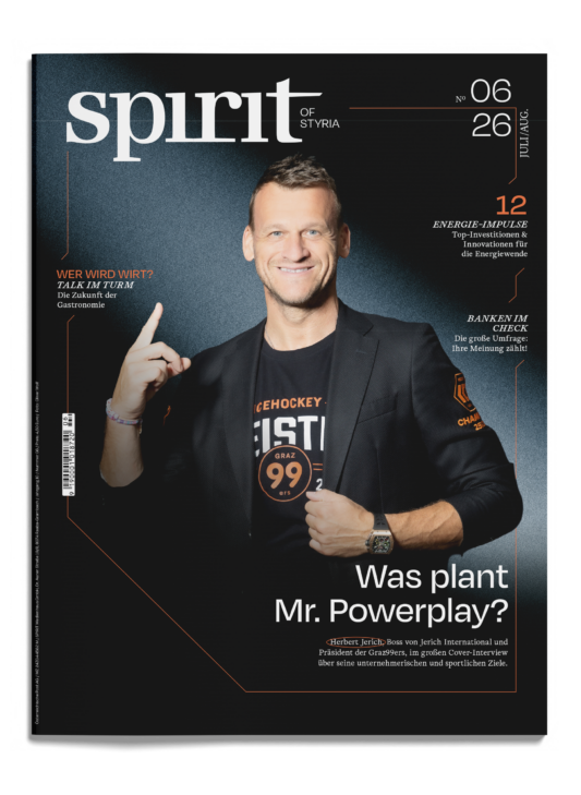 Ein lächelnder Mann im Anzug zeigt auf einem Zeitschriftencover nach oben; die Überschrift lautet: „War Mr. Powerplay ein Spitzel?“; dazu kommen orangefarbene und weiße Textelemente.
