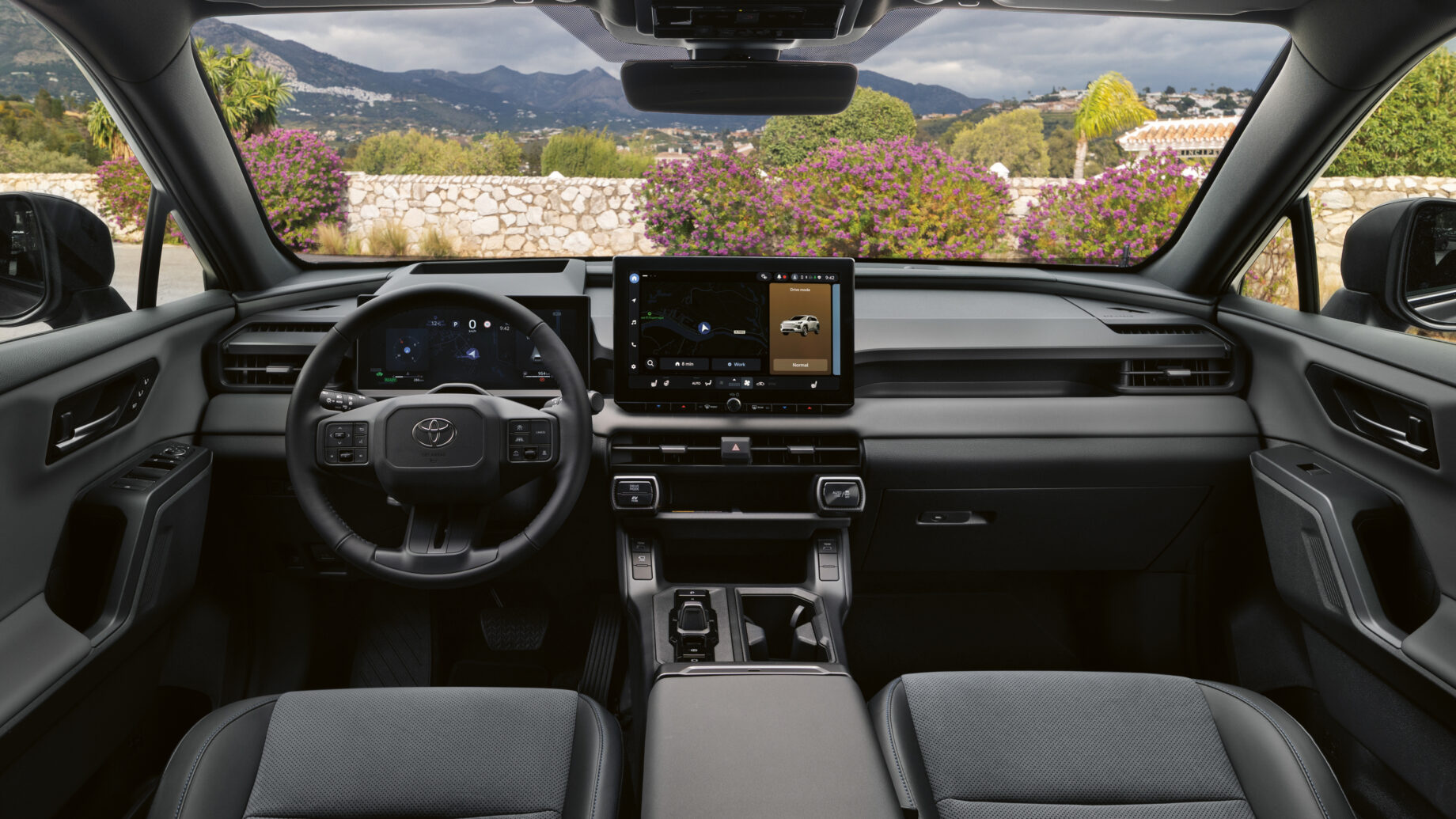 Moderner Fahrzeuginnenraum mit digitalem Armaturenbrett, großem Touchscreen-Display und einer Berglandschaft, die durch die Windschutzscheibe zu sehen ist.