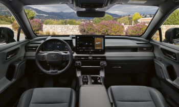 Moderner Fahrzeuginnenraum mit digitalem Armaturenbrett, großem Touchscreen-Display und einer Berglandschaft, die durch die Windschutzscheibe zu sehen ist.