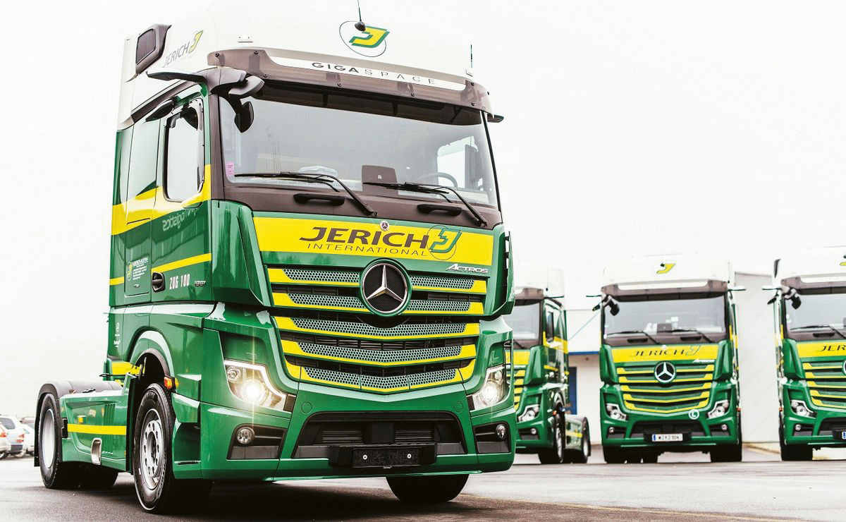 An einem bewölkten Tag stehen die grün-gelben Lkw von Jerich International Mercedes-Benz in einer Reihe und warten auf ihren Transport.