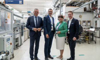 Vier Fachleute in Geschäftskleidung lächeln in einer Industriehalle und verkörpern damit den Geist der steirischen Wirtschaft und des WKO-Wirtschaftsbarometers.