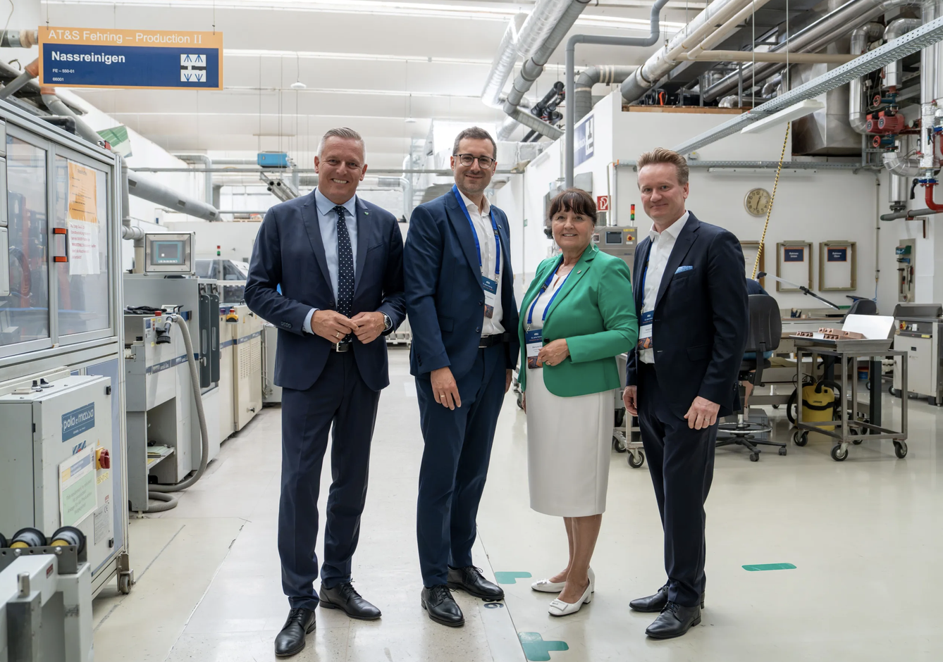 Vier Fachleute in Geschäftskleidung lächeln in einer Industriehalle und verkörpern damit den Geist der steirischen Wirtschaft und des WKO-Wirtschaftsbarometers.