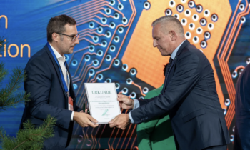 Zwei Männer in Anzügen überreichen sich auf der Bühne eine Urkunde, im Hintergrund ist das Leiterplatten-Design des steirischen WKO-Wirtschaftsbarometers zu sehen.