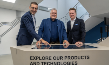 Drei Männer in Anzügen erkunden auf einem Touchscreen Produkte und Technologien und stellen dabei die steirische Wirtschaft sowie das WKO-Wirtschaftsbarometer in den Vordergrund.