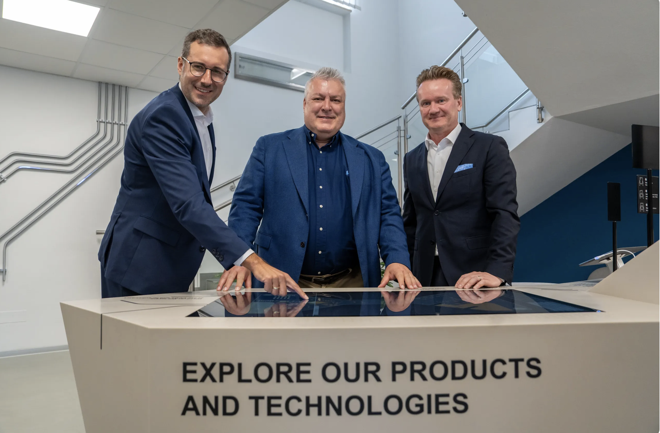 Drei Männer in Anzügen erkunden auf einem Touchscreen Produkte und Technologien und stellen dabei die steirische Wirtschaft sowie das WKO-Wirtschaftsbarometer in den Vordergrund.