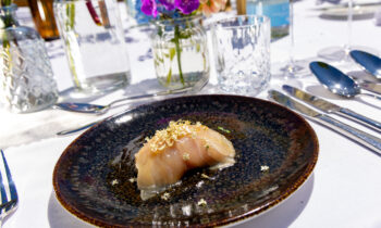 Ein Sushi-Gericht, garniert mit Goldflocken auf einem dunklen Teller, serviert auf einem eleganten Tisch mit Blumen, Gläsern und Besteck.