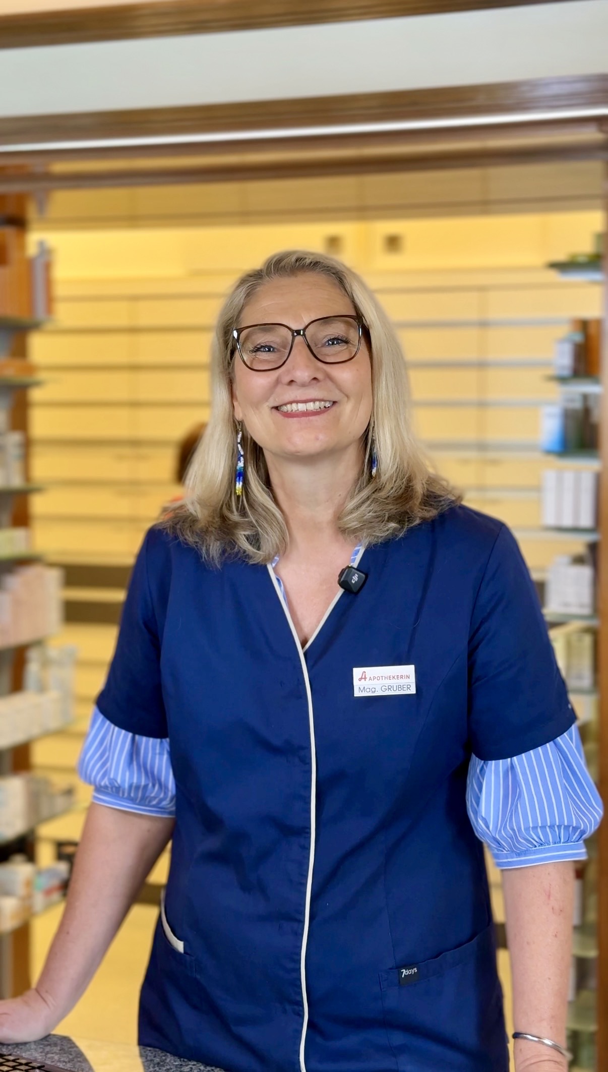 Ilse Gruber aus Köflach: Eine Kandidatin beim "ApothekenStar 2026-Voting" steht lächelnd in ihrem blauen Kittel in ihrer gut sortierten Apotheke.