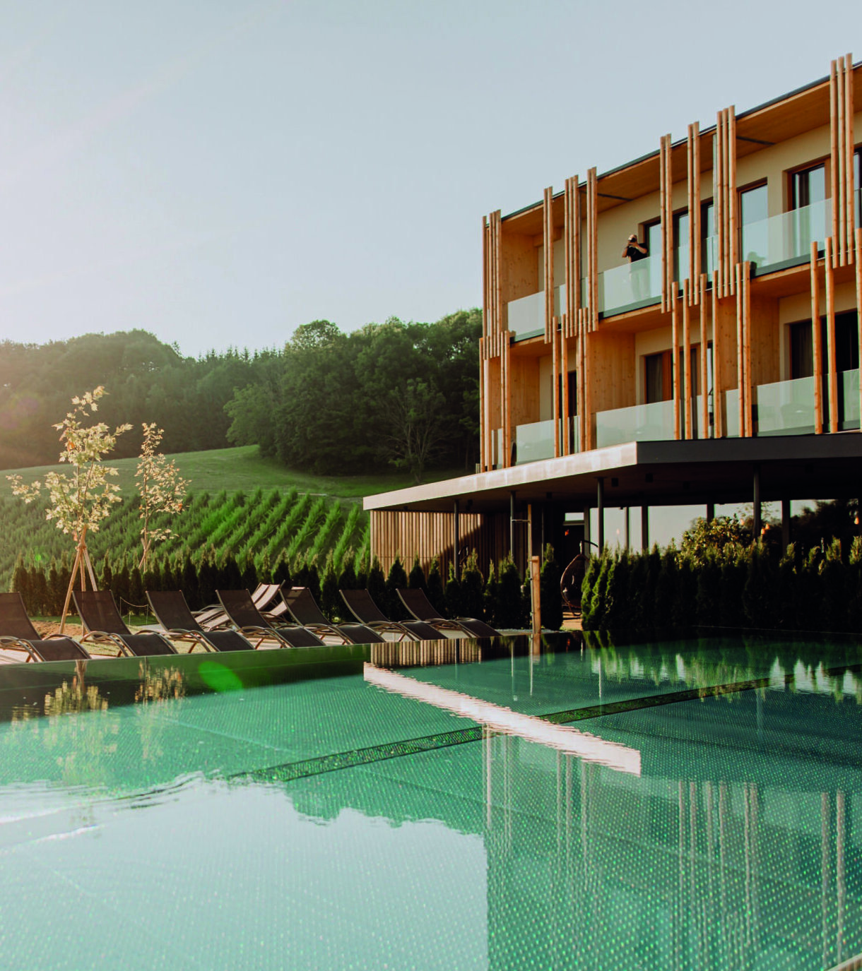 Sonnenaufgang über dem modernen Hotel von Apotheker-Wahl mit Außenpool, Liegestühlen und grünen Hügeln im Hintergrund.