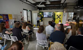 Ein Mann hält vor einem sitzenden Publikum beim Raiffeisen-Agrarsymposium einen Vortrag; auf einer Leinwand in einem modern eingerichteten Raum ist eine Folie mit der Aufschrift „70 %“ zu sehen.