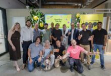 Eine Gruppe von sechzehn Personen und einem Hund lächelt in einem modernen Raum mit Luftballons, einem Banner mit der Aufschrift „Humantech Demo Day“ und einer Atmosphäre, die an das Raiffeisen-Agrarsymposium erinnert.