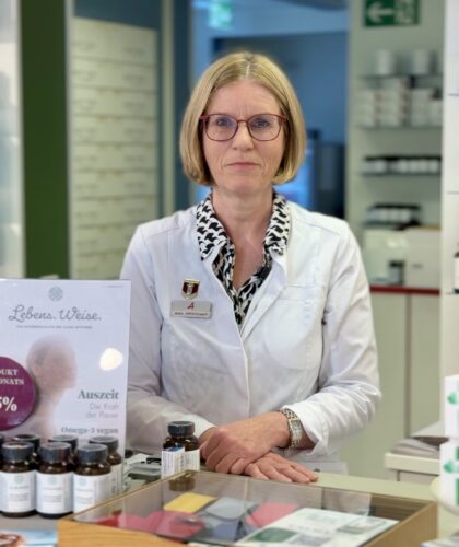 Sonja Kirschner steht in einem weißen Kittel hinter der Theke mit Informationsschildern.