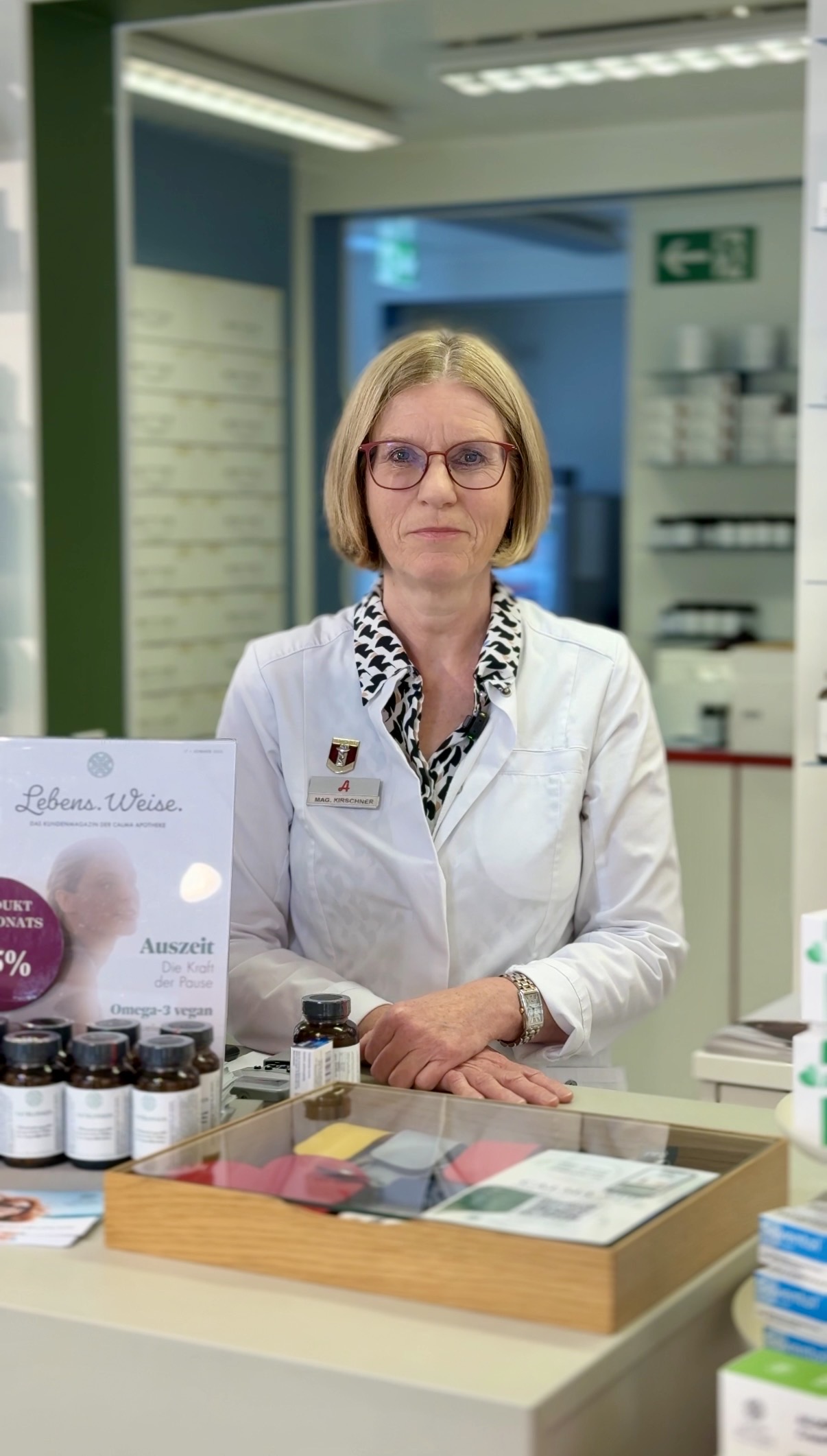 Sonja Kirschner steht in einem weißen Kittel hinter der Theke mit Informationsschildern.