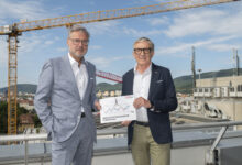 Zwei Männer in Anzügen stehen mit einer Karte auf einem Dach, während sich hinter ihnen Kräne erheben – Siemens Mobility eröffnet einen 40-Millionen-Euro-Hub in Fürstenfeld.