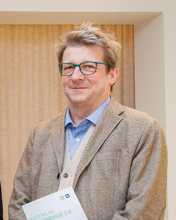 Fünf Männer in Anzügen stehen in einem Raum, lächeln und halten aufgeschlagene Zeitschriften mit einem grünen Natur-Titelblatt in den Händen. An der Wand hinter ihnen hängt ein gerahmtes abstraktes Gemälde.